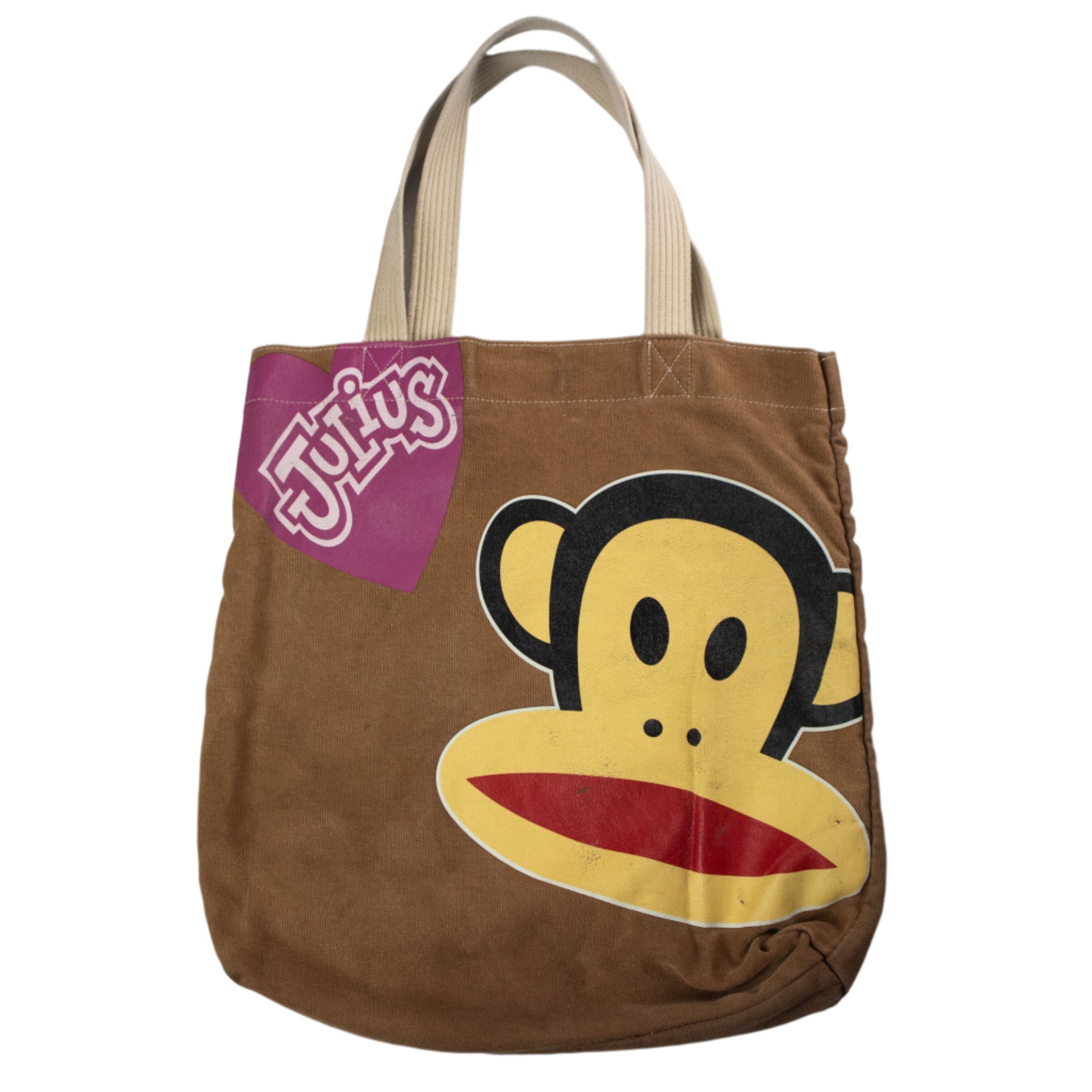 Brown tote bag with a cartoon monkey face design and a pink tag on a white background