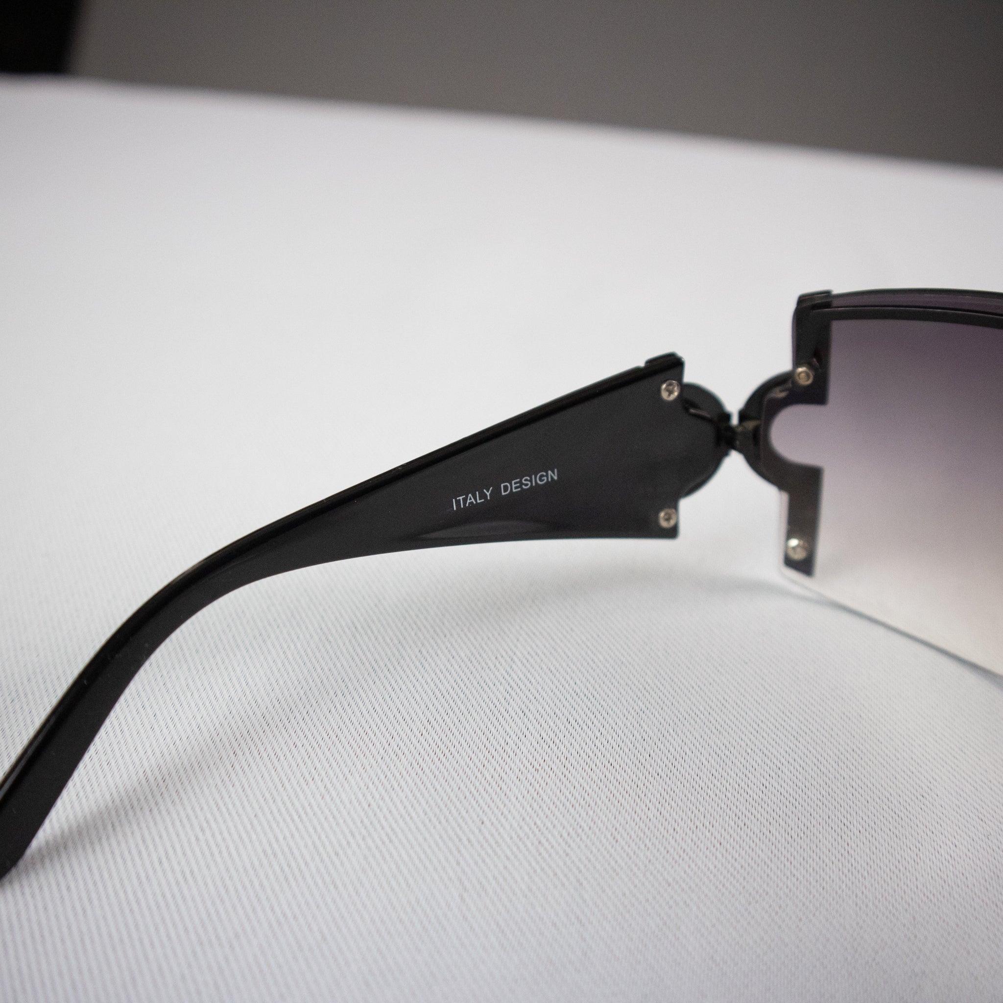 Black sunglasses with 'Italy Design' on the frame, lying on a white surface.