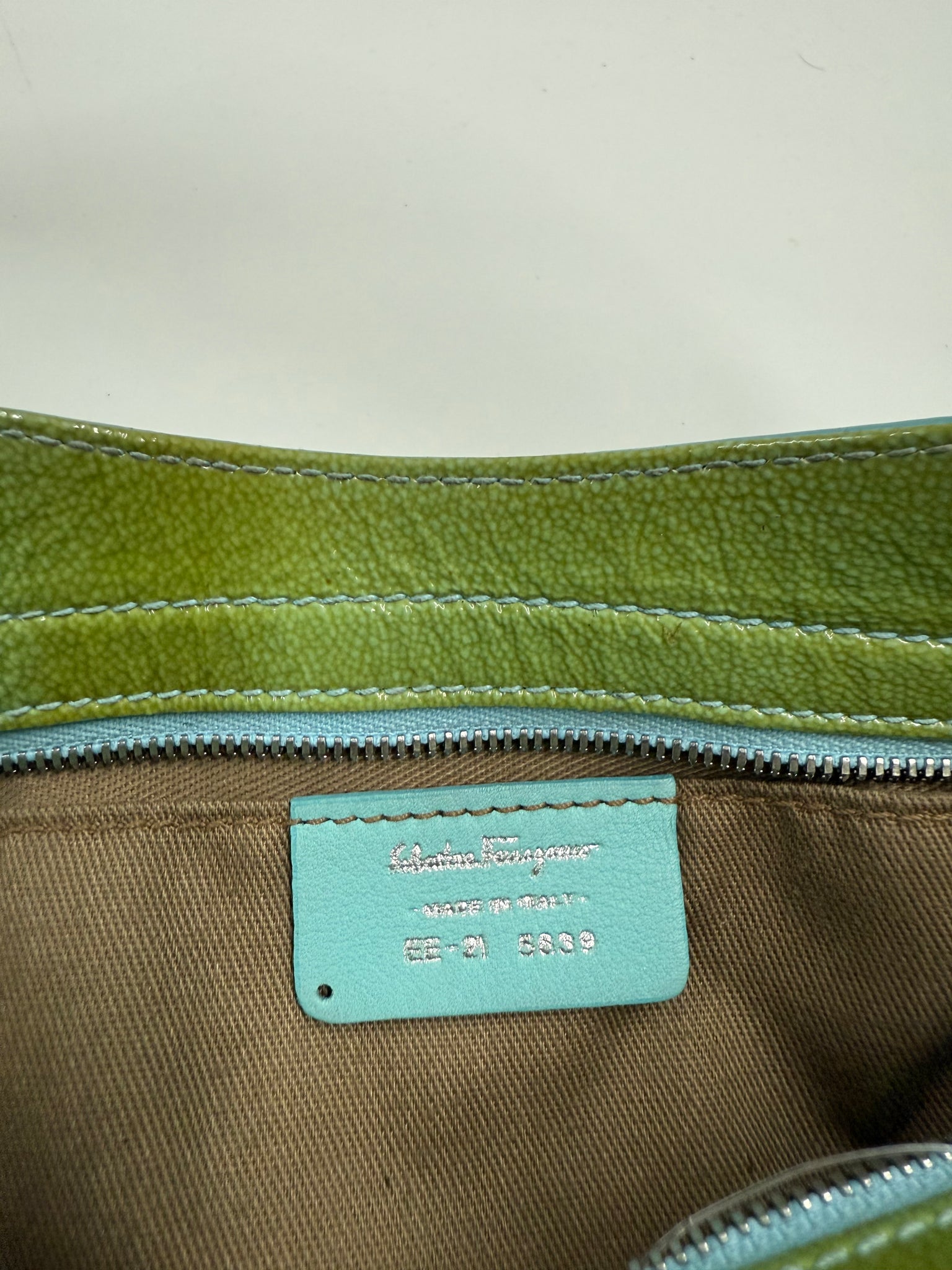 Close-up of a green zipper on a brown fabric background with a visible brand label.