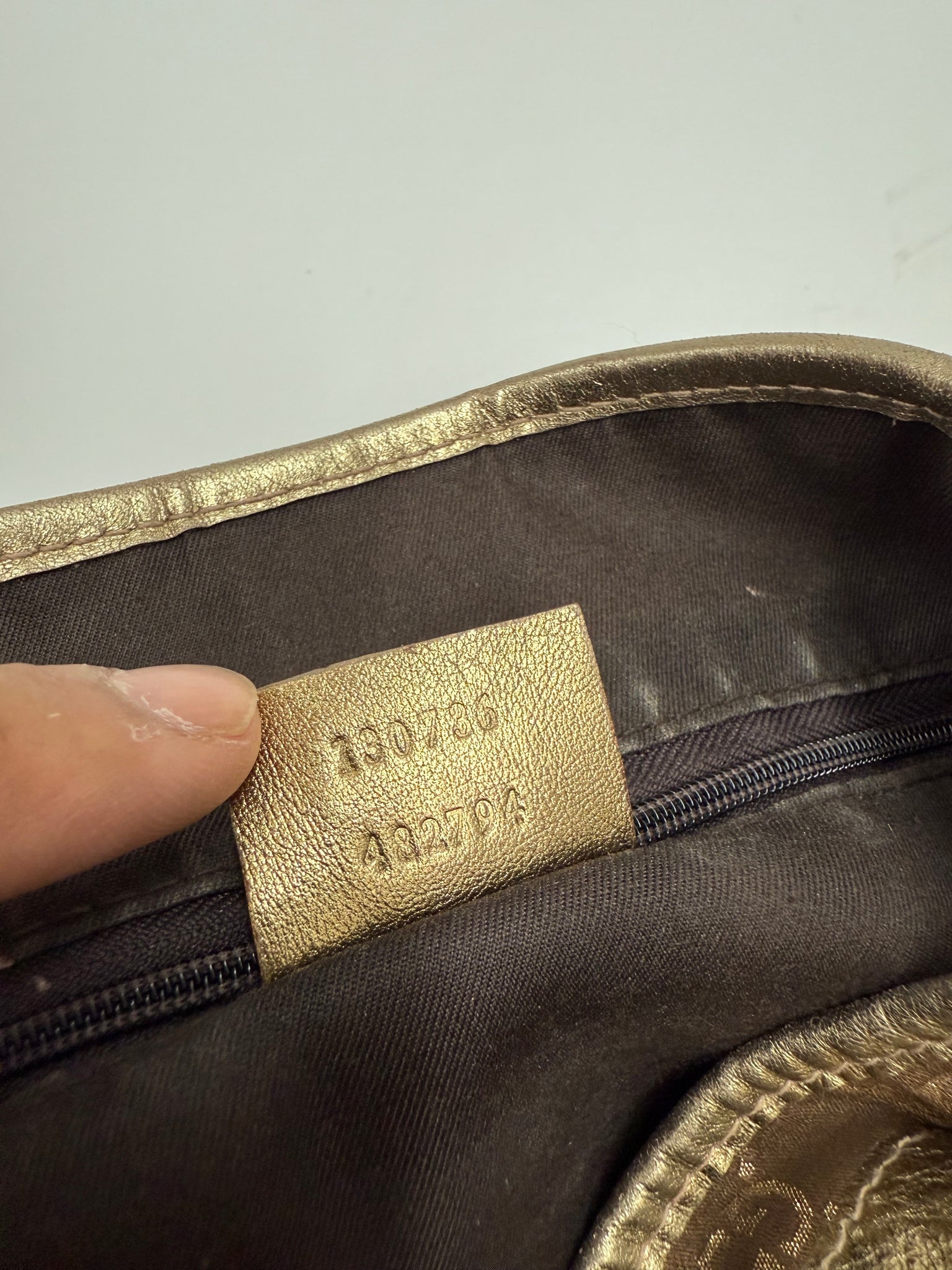 Brown patterned bag on a white background gucci hang bag gold design with iconic pattern high end designer luxury authentication number close up tag