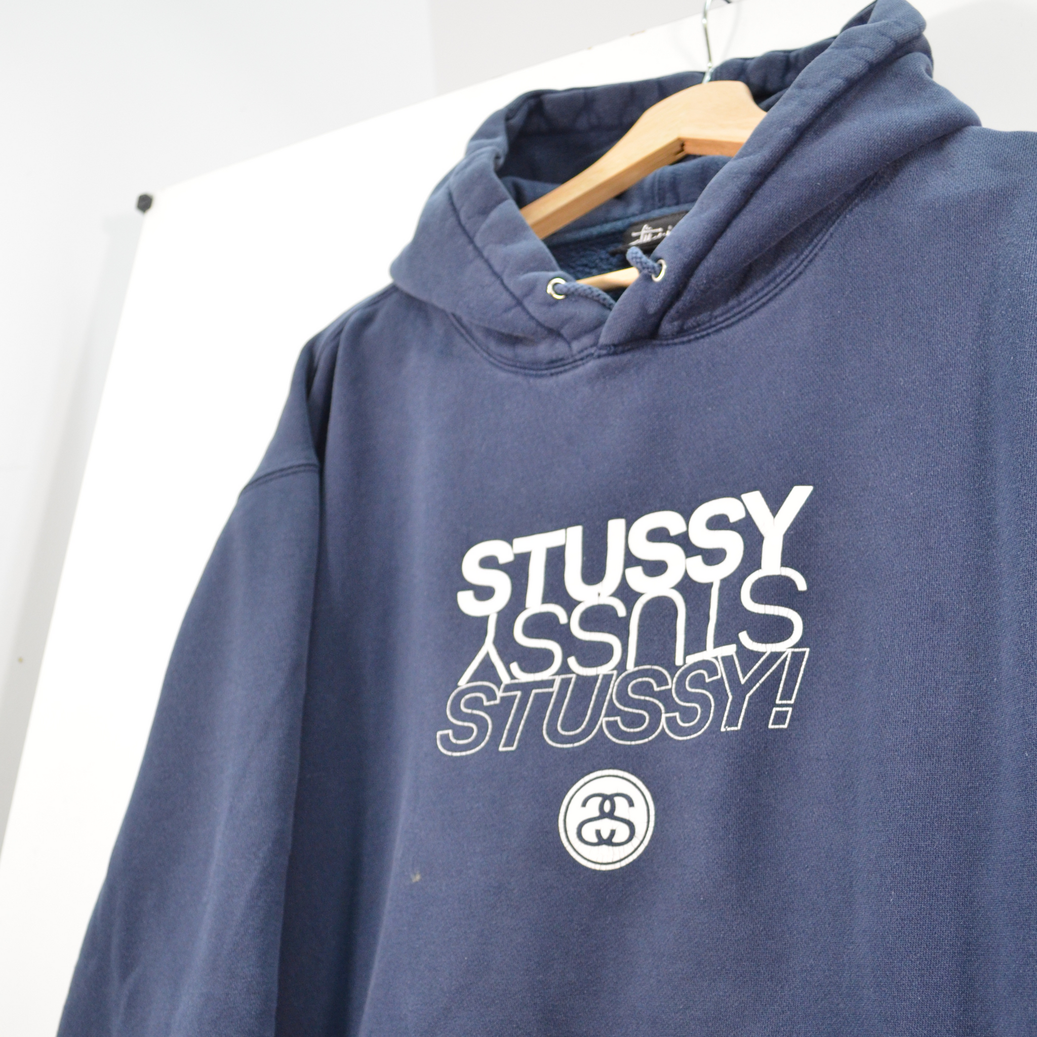 Navy blue hoodie with 'Stussy' logo on a hanger against a white background